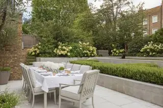 Ideen für Terrassenmöbel für den Außenbereich mit einem langen, mit weißem Leinen gedeckten Tisch in einem Stadtgarten mit weißen Hortensien.