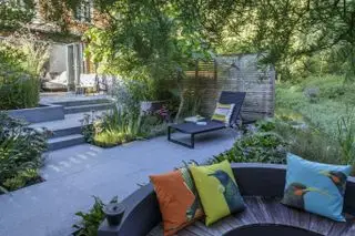 Ideen für versenkte Terrassenmöbel in einem schattigen, grau gepflasterten Garten mit überhängenden Bäumen.