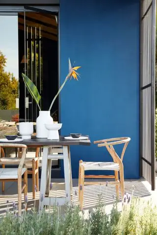 Ideen für Terrassenmöbel aus Holz aus der Mitte des Jahrhunderts vor einer leuchtend blau gestrichenen Wand.