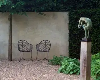 Escultura sobre un pedestal junto al muro de un jardín.