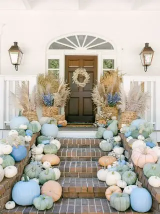 Decoração de porta de Halloween com abóboras azuis pastel, verdes e laranja claro que levam até a porta da frente e varanda, pampas em cestos, guirlanda na porta