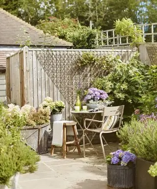 En solrik terrassehage med et lite sett med bord og stoler, omgitt av beplantning inkludert lavendel og hortensia