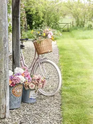 Bauerngarten mit Kiesweg und Rasen und Fahrrad und Blumen in Eimern