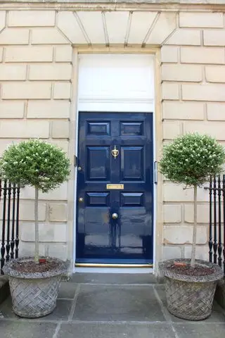 casa georgiana con puerta azul y dos laureles estándar a cada lado de la puerta en macetas de piedra