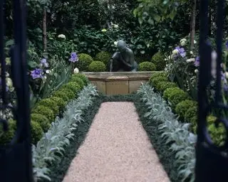 Camino del jardín que conduce a la estatua con repetidas plantaciones de buxus, stachy y hortensias en ambos lados.