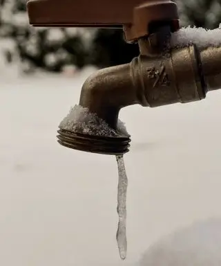 Eine kleine Menge Wasser, die an der Spitze eines Wasserhahns zu einem Eiszapfen gefroren ist