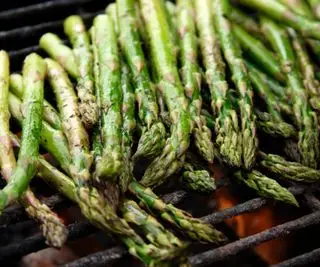 Un primer plano de espárragos casi terminados de cocinarse en una parrilla de carbón