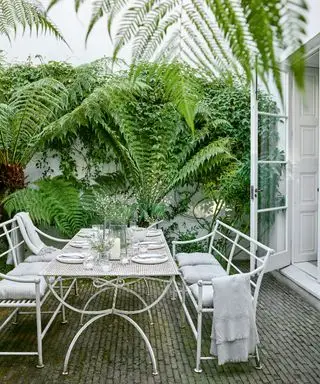 Gartenterrasse mit weißem, zum Mittagessen gedecktem Tisch und Stühlen