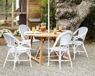 Et cirkulært træhavebord omgivet af udendørs spisestole i rattaneffekt
