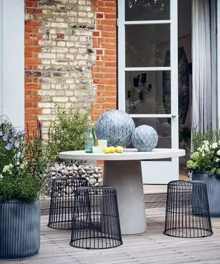 Idee per un ampio giardino sul balcone con tavolo rotondo e sgabelli in filo metallico.