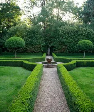 parterre de setos de boj con caminos de grava alrededor de una fuente y una estatua en el otro extremo