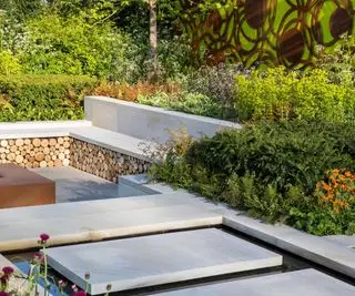 Lajes de pedra Yorkstone sobre um elemento aquático que leva a um jardim submerso com banco de pedra e arbustos