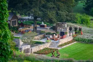 Un jardín paisajístico con césped junto a un comedor con escalones de piedra y una pared.