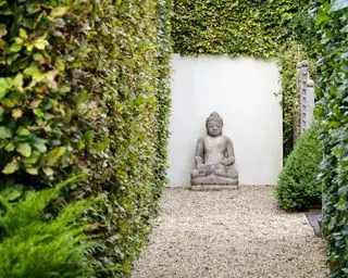 En Buddha-statue i enden av en lang grussti med hekker.