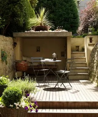 Idéer til haveafskærmning illustreret af et overdækket opholdsområde med terrasse og bistrobord og stole.