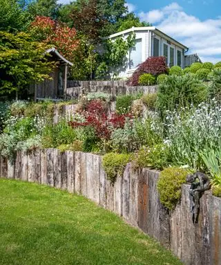 Et terrasseret beplantningsområde med rustikke trælag og beplantning i stenstil.