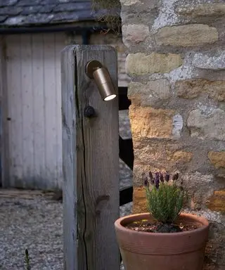 Detailní záběr reflektoru svítícího na květináč s levandulí před cihlovou zdí