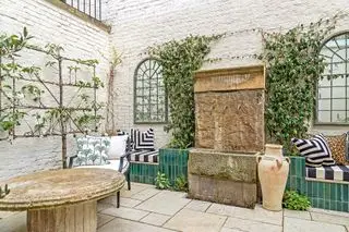 Patio con jardín con paredes blancas, espejos, árboles frutales en espaldera y elementos de piedra recuperada