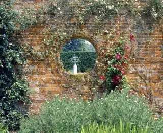 El reloj de sol en Polesden Lacey, Surrey, visto a través de un portal circular en el muro de un jardín
