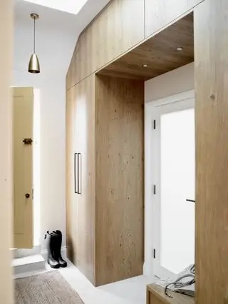 Pasillo/entrada con almacenaje incorporado de madera, suelo blanco, alfombra, lámpara colgante y paredes blancas.