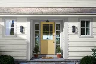 Exterior de la casa con revestimiento blanco y puerta de entrada acristalada pintada de amarillo
