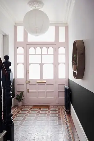 Pasillo con piso de baldosas, pared inferior en negro y superior en blanco y puerta de entrada pintada en rosa pálido.