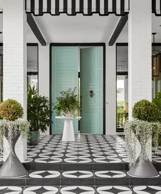 Puerta de entrada de color azul pálido con porche de azulejos blancos y negros