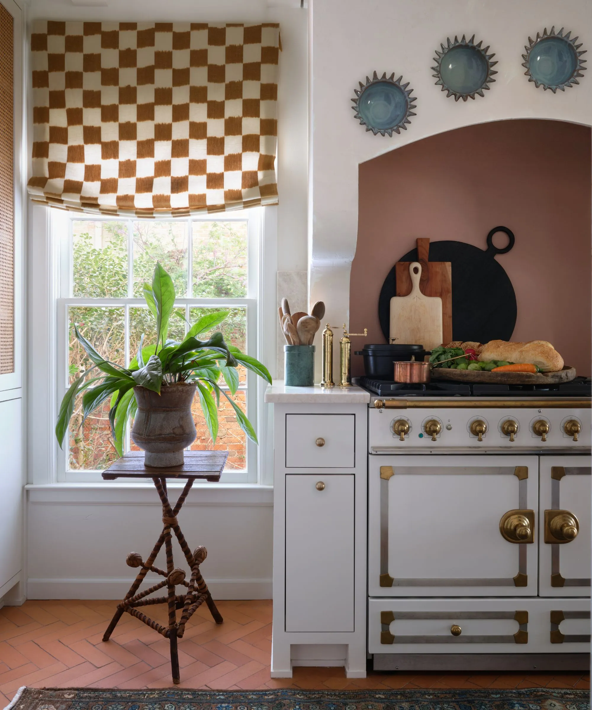 Um detalhe de cozinha brilhante com uma linha de estilo vintage em branco e latão, uma persiana romana xadrez e um piso de cerâmica de terracota' loading='lazy' title=