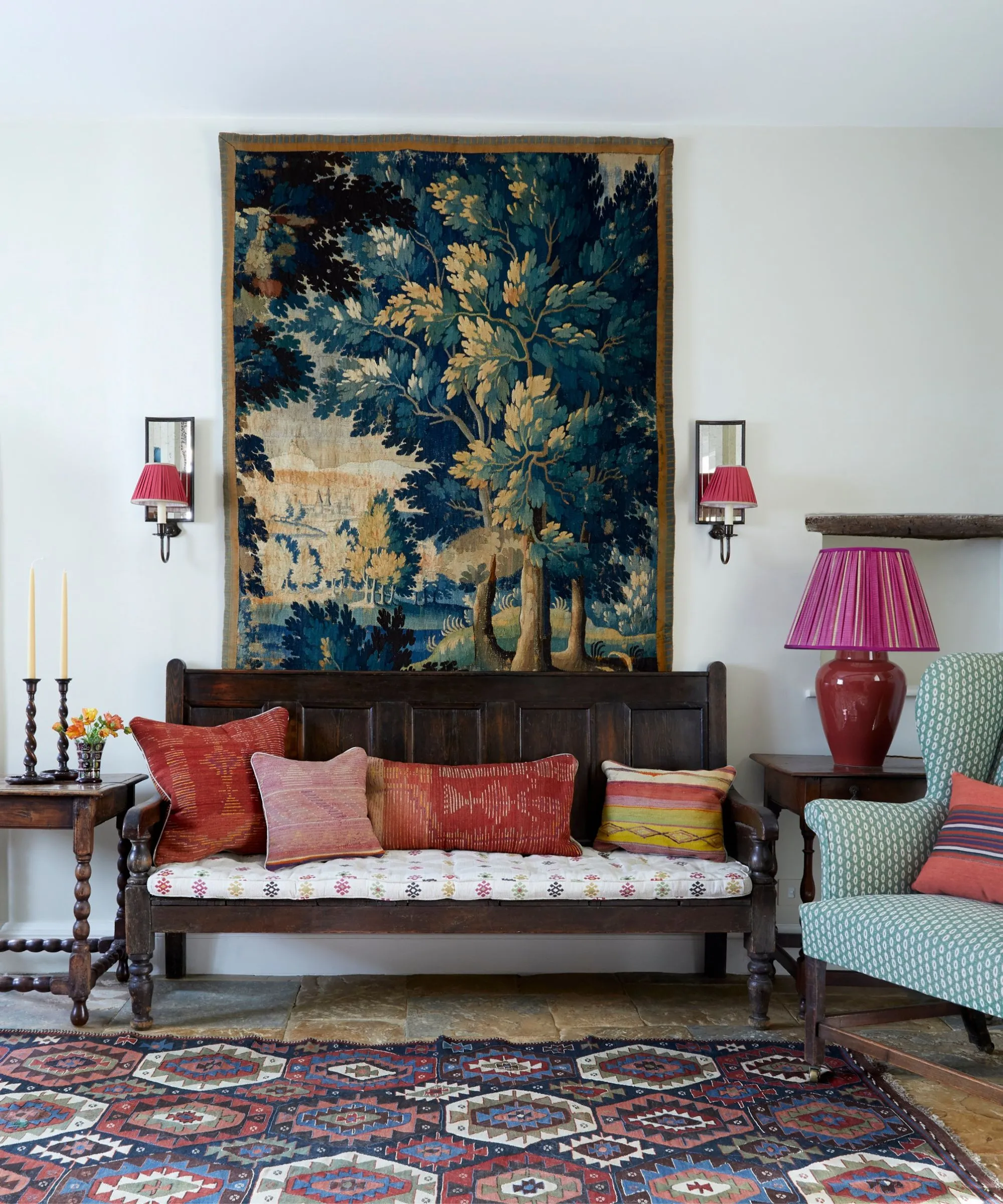 Una entrada rústica con un banco de madera oscura con cojines rojos, un gran tapiz con motivos de árboles y una vibrante alfombra geométrica.' loading='lazy' title=