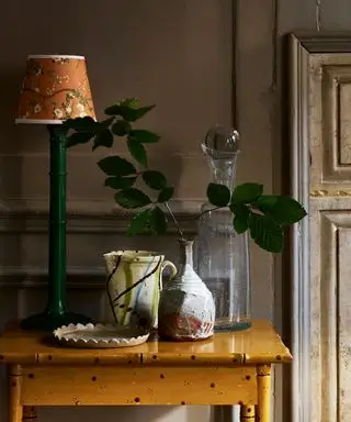 Okkergul malet sidebord med grøn bordlampe, gul dekorativ skærm og keramiske kar