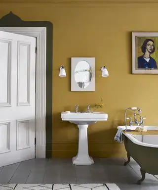 Efterårsfarver i et badeværelse med gule okker vægge, hvid vask og gråt badekar