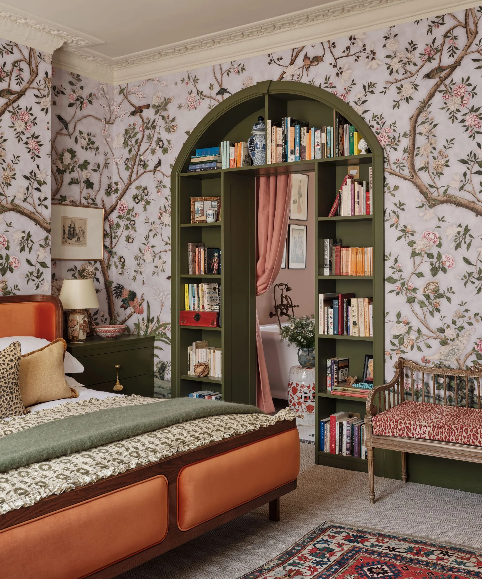 Blumenwandtapete in einem Schlafzimmer mit einer Tür zum Hauswirtschaftsraum mit dunkelgrünem Bücherregal, Regalen, rosa Vorhängen und einem orangefarbenen Bett' loading='lazy' title=