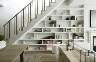 Kælder med trappe og skræddersyede reoler under, bord trægulv, tæppe, konsolbord og sofa