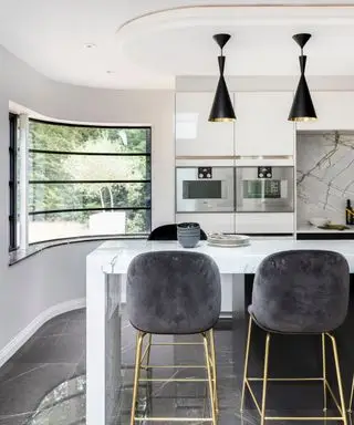 Une cuisine d'inspiration art déco avec des fenêtres incurvées, un îlot et des plafonniers noirs