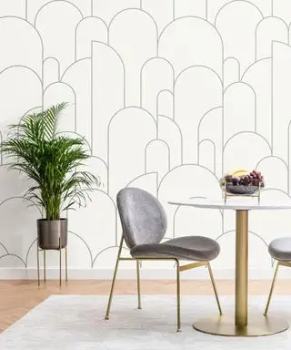 Une salle à manger avec une table blanche et dorée, une chaise grise, un papier peint végétal et géométrique