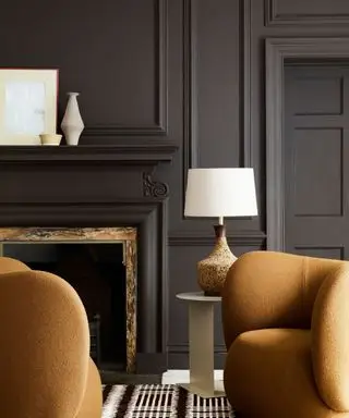 Ein farbenfrohes Zimmer in Schwarz mit zwei hellbraunen Stühlen, einer weißen Tischlampe und einem schwarz gestrichenen Kaminsims