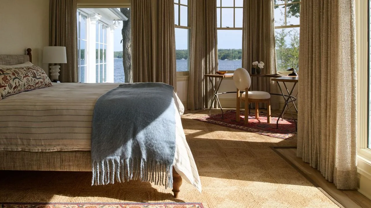 Ložnice s neutrálním barevným schématem a velkými okny s pudrově modrým přehozem na posteli.' loading='lazy' title=