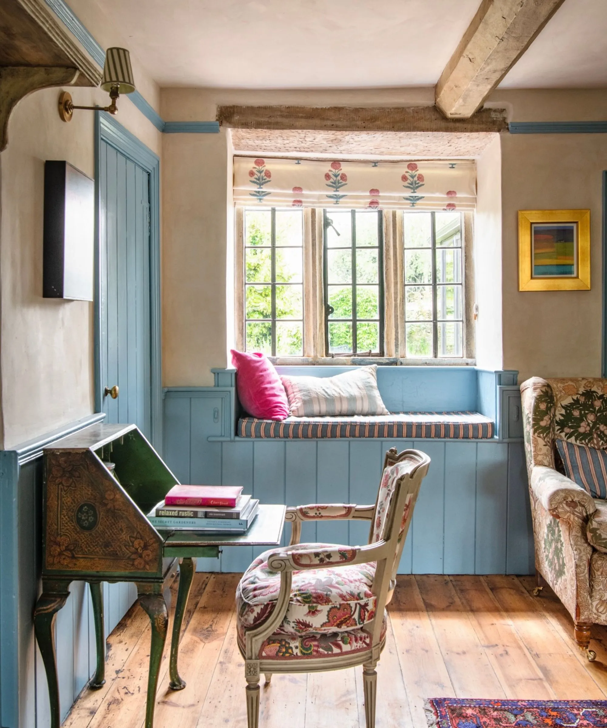 Rustikální obývací pokoj s dřevěnými stropními trámy lemuje okno s okenním sedákem a modrým obložením.' loading='lazy' title=