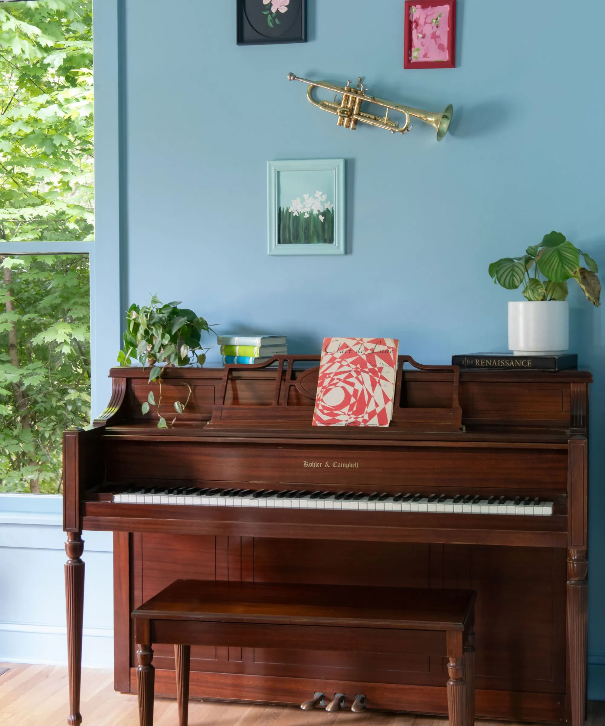 Modrou barvou prosáklý pokoj s dřevěným klavírem a galerijní stěnou nad ním.' loading='lazy' title=