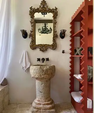 Baño de decoración mexicana con estanterías rojas y lavabo de piedra.