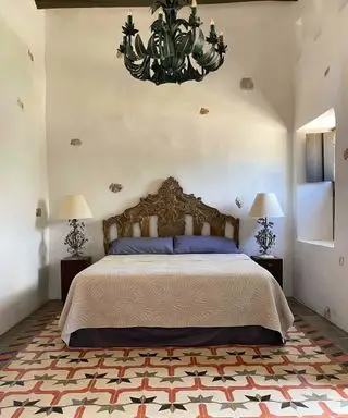 Dormitorio con decoración mexicana, cama con estructura oscura y lámpara de araña.