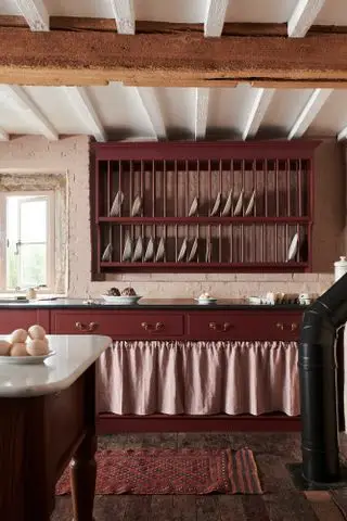 Cocina tradicional de color burdeos con gabinetes pintados y estante para platos.
