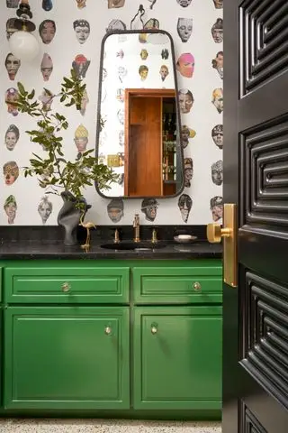 cuarto de baño con mueble verde, papel pintado retro, espejo retro, encimeras negras, grifos de latón