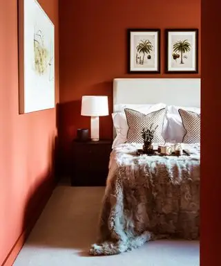 Un dormitorio rojo anaranjado con cabecera blanca y ropa de cama color crema.