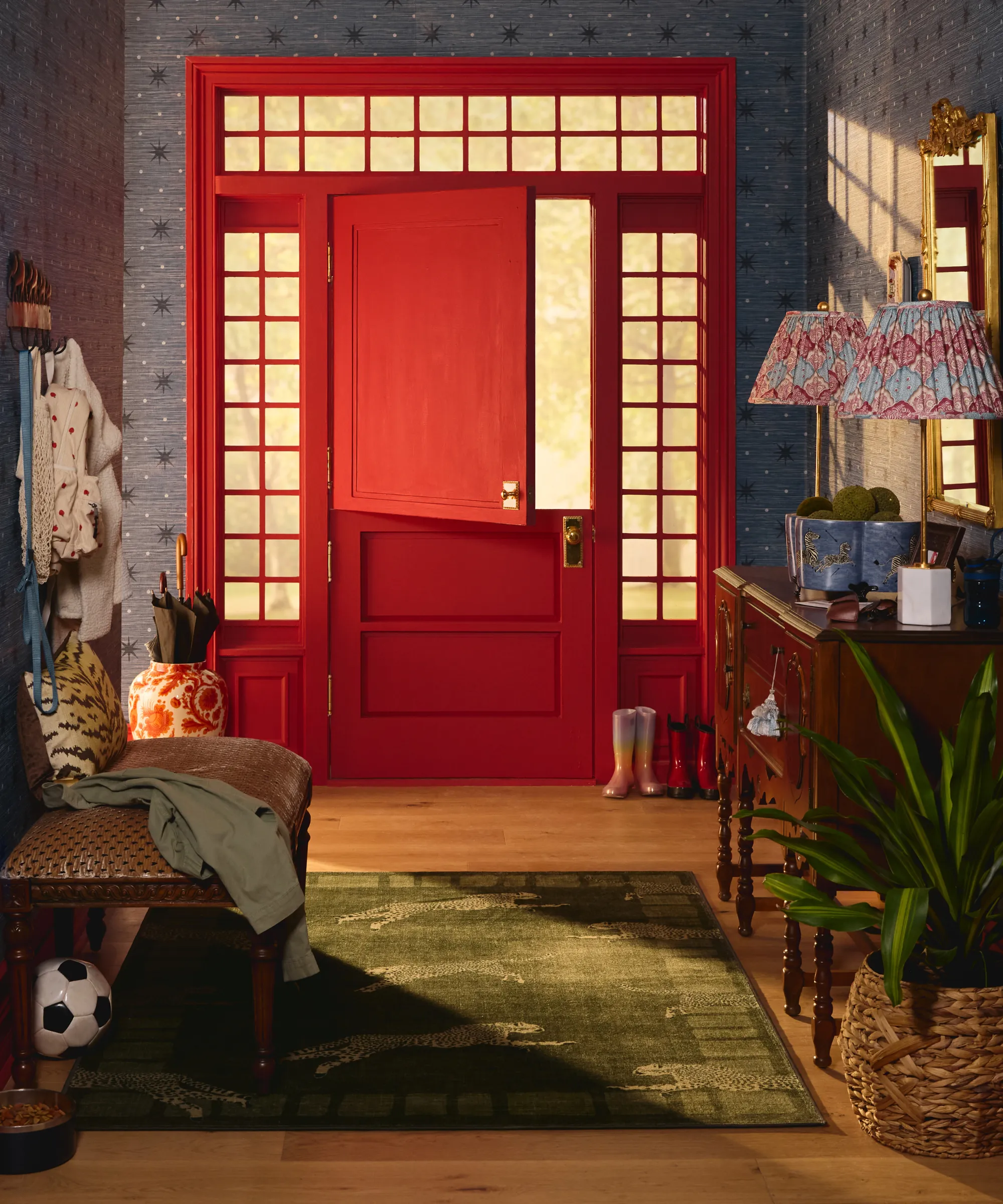 una entrada con un papel tapiz azul de puerta holandesa de color rojo brillante una mesa consola en la entrada con dos lámparas encima y una alfombra en la entrada' loading='lazy' title=