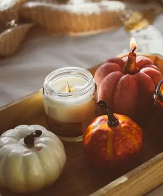 Uma vela apagada em uma bandeja de madeira ao lado de uma pequena abóbora e uma vela acesa em forma de abóbora