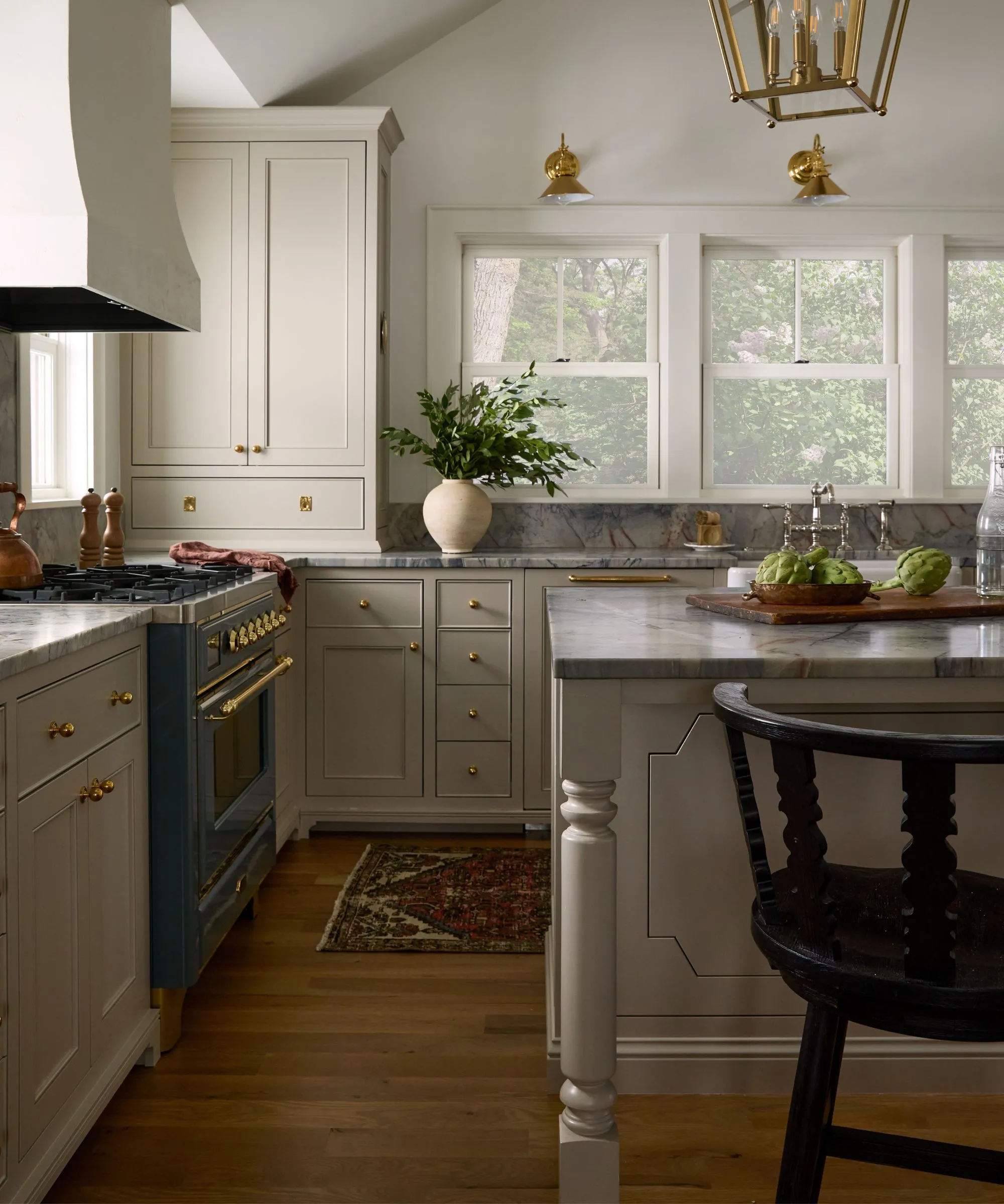 zemitá neutrální kuchyně s velkými okny s výhledem na jezero, velkým sádrovým odsavačem par a pracovními deskami z modrého mramoru' loading='lazy' title=