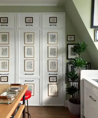 Cocina pintada de verde con mesa de madera y puertas de almacenaje con paneles y obras de arte.