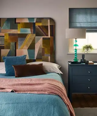 Dormitorio con cama y cabecero, mesita de noche y lámpara de mesa.
