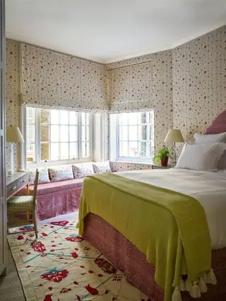 papel tapiz floral con la misma tela en persianas, combinación de colores verde y rosa, alfombra, tocador, asiento junto a la ventana
